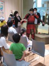 甲冑の複製を着た図書館職員と甲冑の仕組みを説明する学芸員