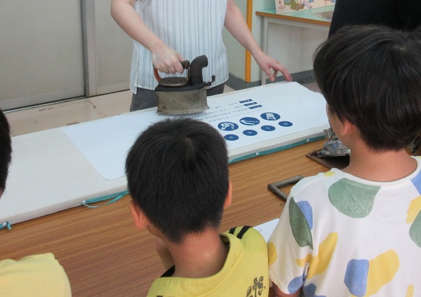 学芸員が炭火アイロンをあてているのをみる子ども